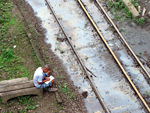 Homem faz palavras cruzadas sentado  beira da linha de trem, enlameada, no porto de Santos